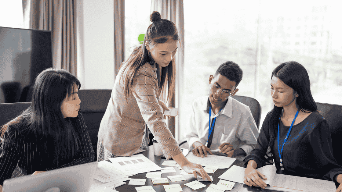 Office leader pointing to documents in meeting room with team watching