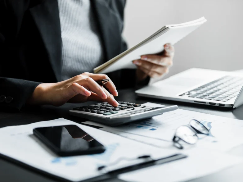 A person in a business suit calculates numbers using a calculator at a desk.