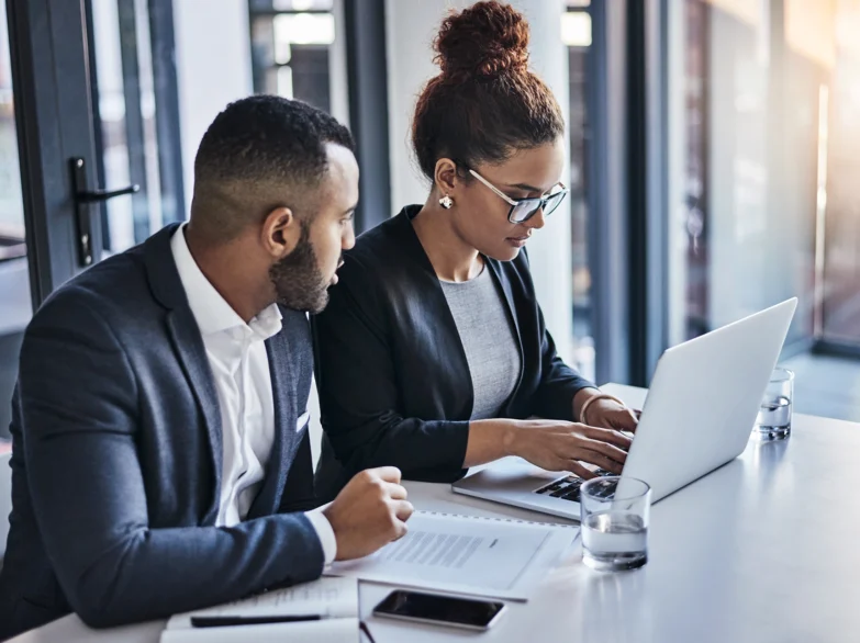Two business professionals collaborating on a laptop, discussing ideas and sharing insights in a modern office setting.