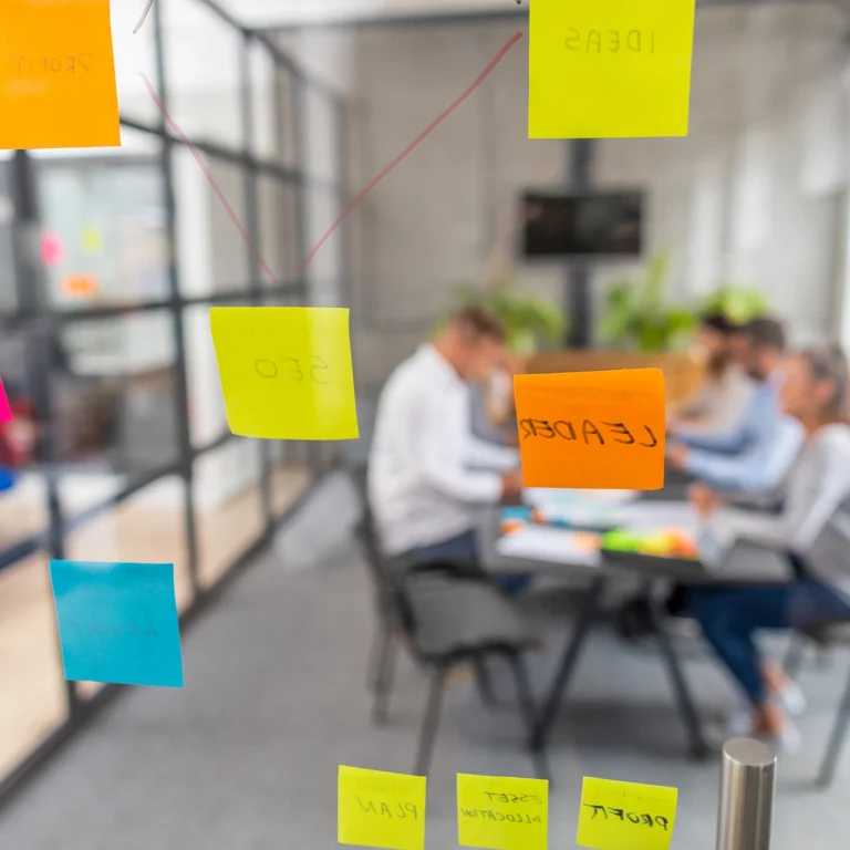 A diverse group of people collaborating around a table, the foreground window is covered in colourful sticky notes.