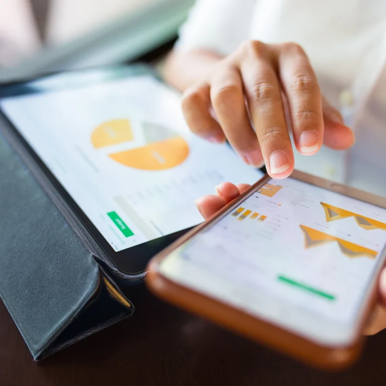 A person holding a tablet in one hand and a smartphone in the other, looking engaged with both devices.