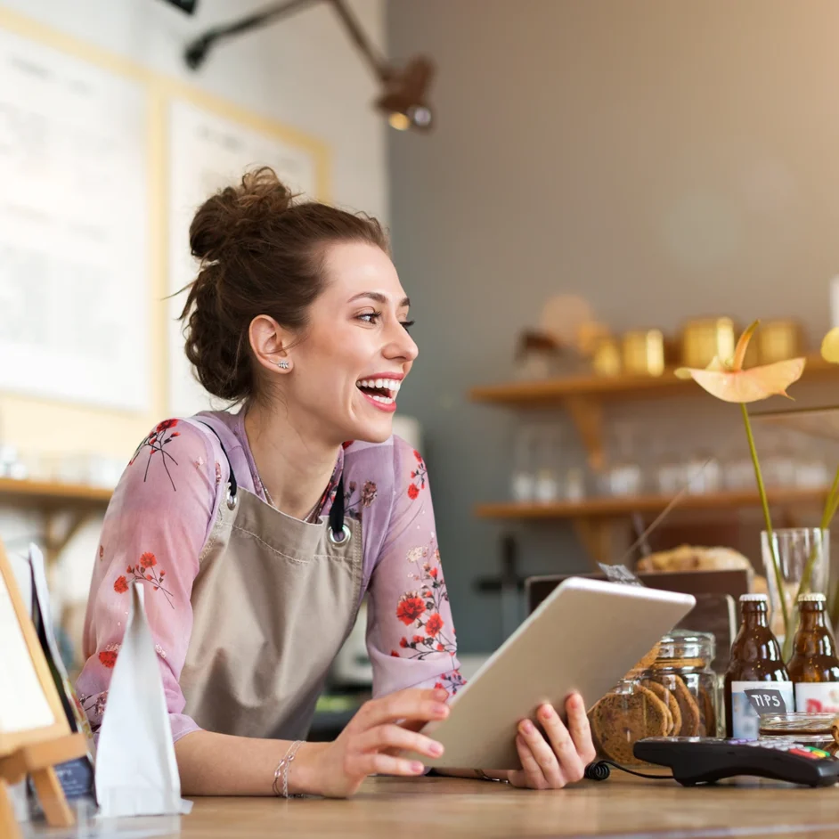 A woman sits at a table, focused on her tablet in her cafe business.