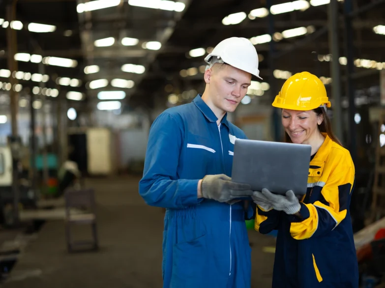 Two people in hard hats collaborating over a laptop, discussing plans or project details.