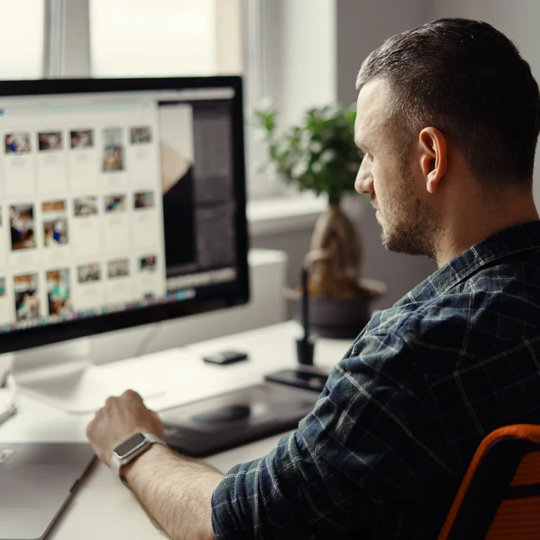 A man sits at a desk with a desktop computer and a laptop, focused on his work.
