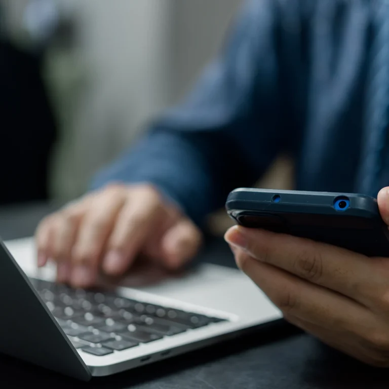 A person holding a cell phone in one hand and a laptop in the other, engaged in multitasking.