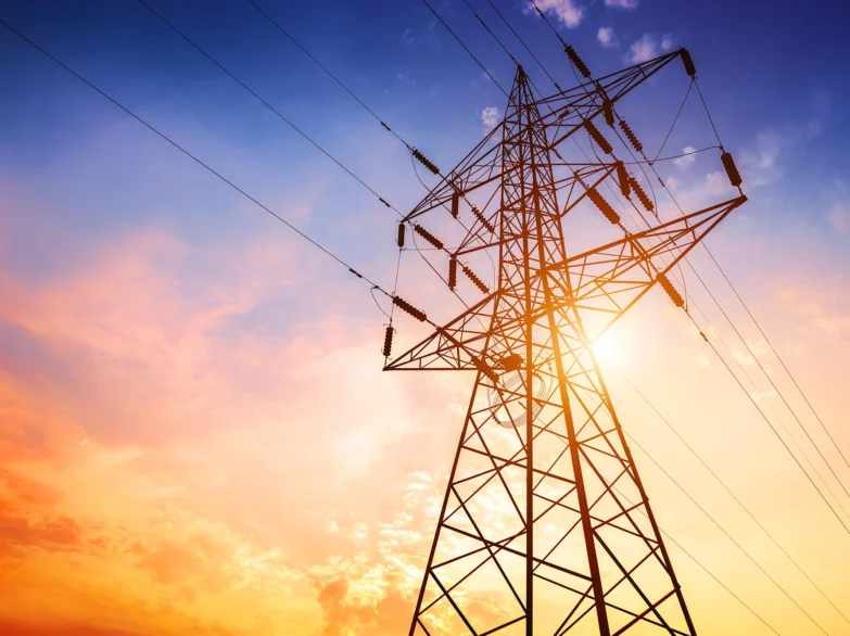 High voltage electricity pylon silhouetted against a vibrant sunset sky.