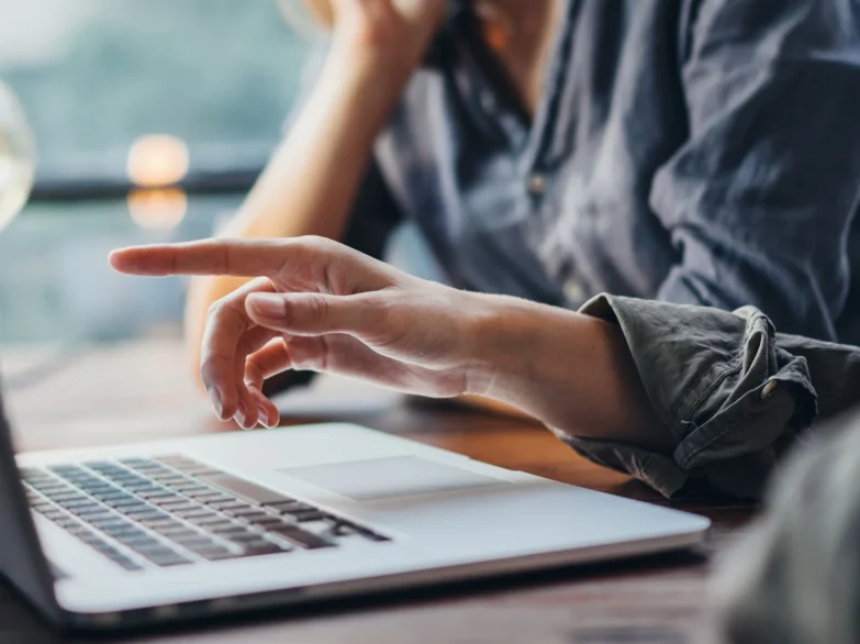A woman points at a laptop on a table, engaging with the screen's content.