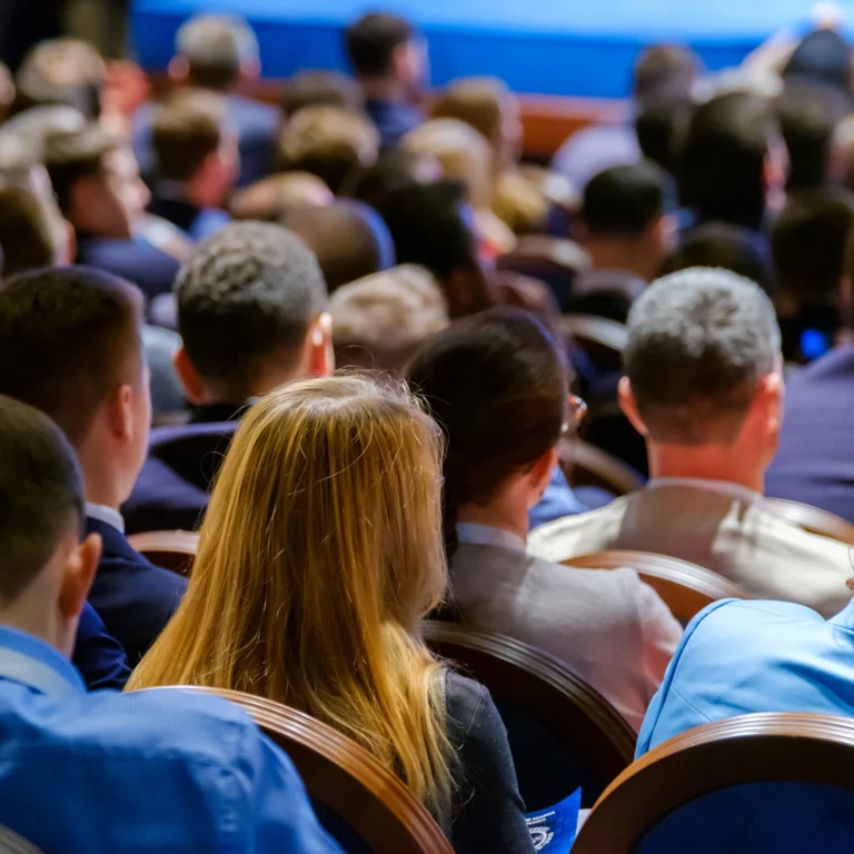 A large crowd of people seated in chairs, attentively listening at a conference event.