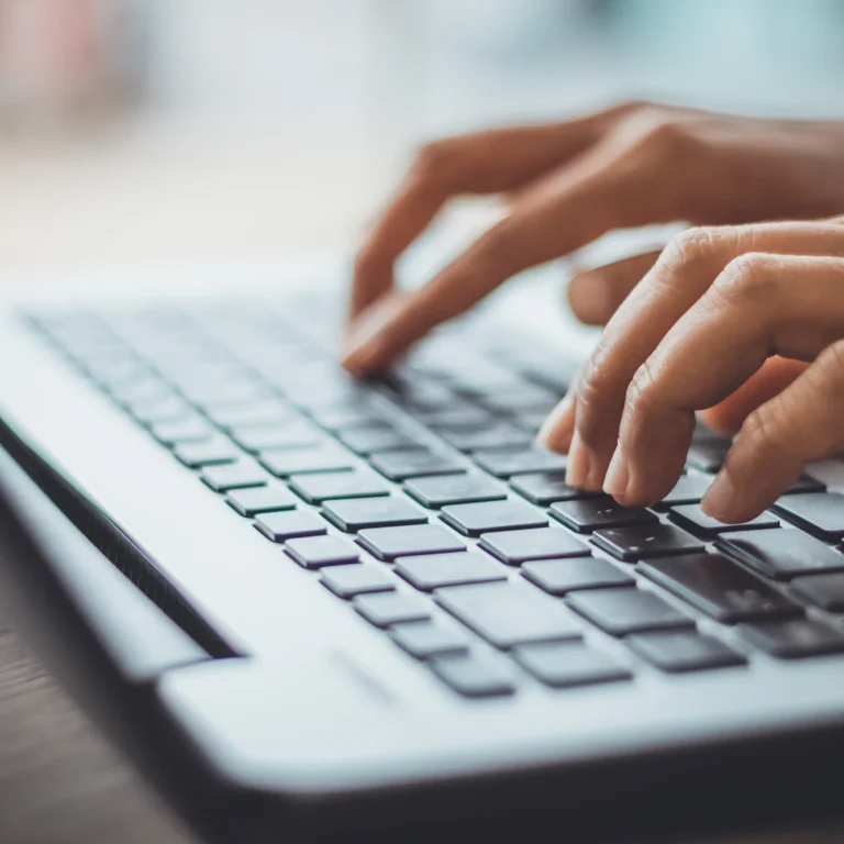 A person focused on typing on a laptop keyboard, with hands positioned over the keys.
