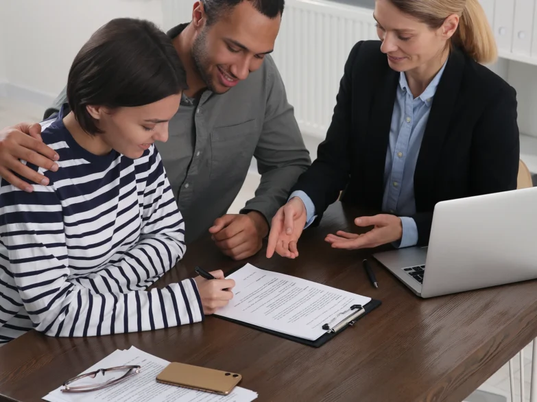 A couple and a man and woman are seated at a table, signing paperwork together.