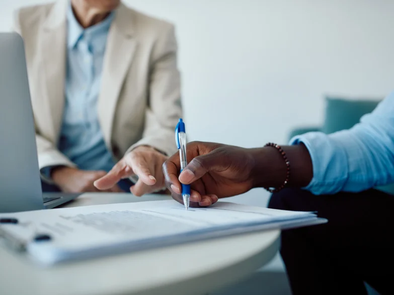Two people sitting at a table, working together with a laptop and a pen.