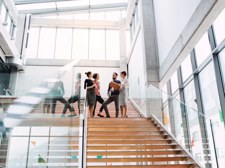 Four people standing on a stairway in an office building, engaged in conversation and looking at each other.
