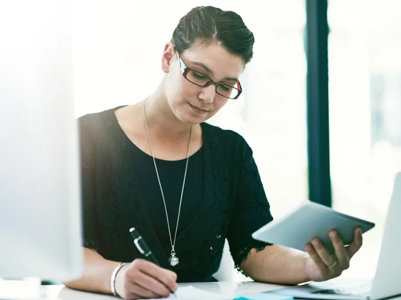 A woman wearing glasses is focused on her laptop, working intently at a desk.