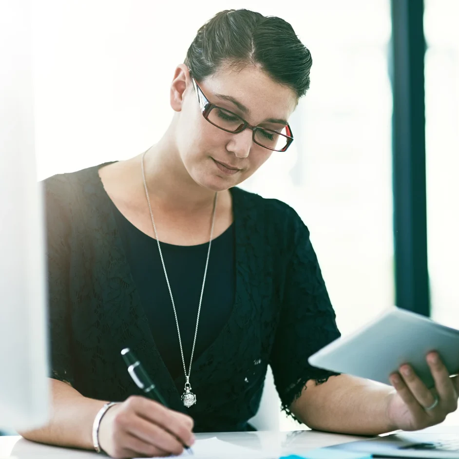 A woman wearing glasses is focused on her laptop, working intently at a desk.