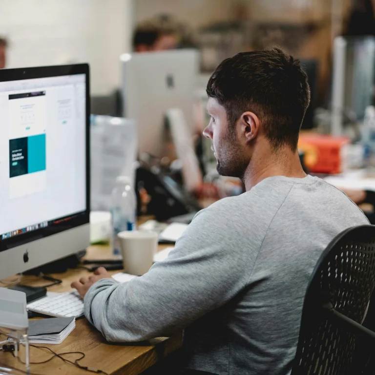 A man focused on his computer while working in a modern office setting, designing content.