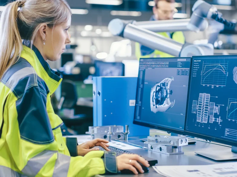 A woman in a safety vest is focused on her work while using a computer at a desk.