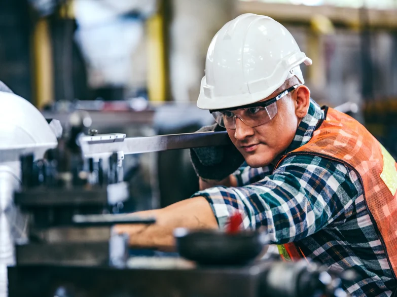 A man in a hard hat operates a machine, focused on his work in a construction or industrial setting.