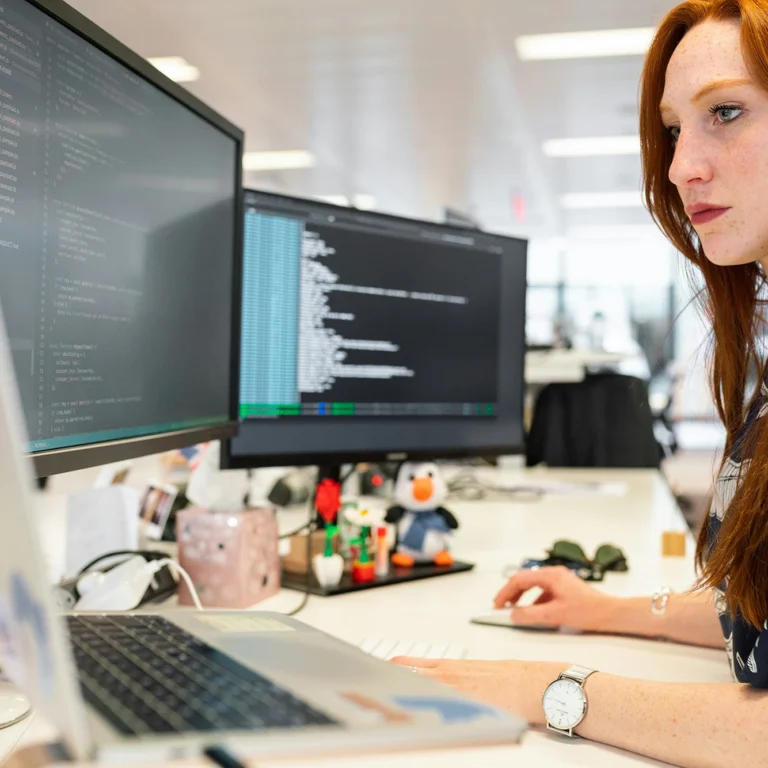 A woman with red hair focused on her work at a computer, typing and engaged in her task.