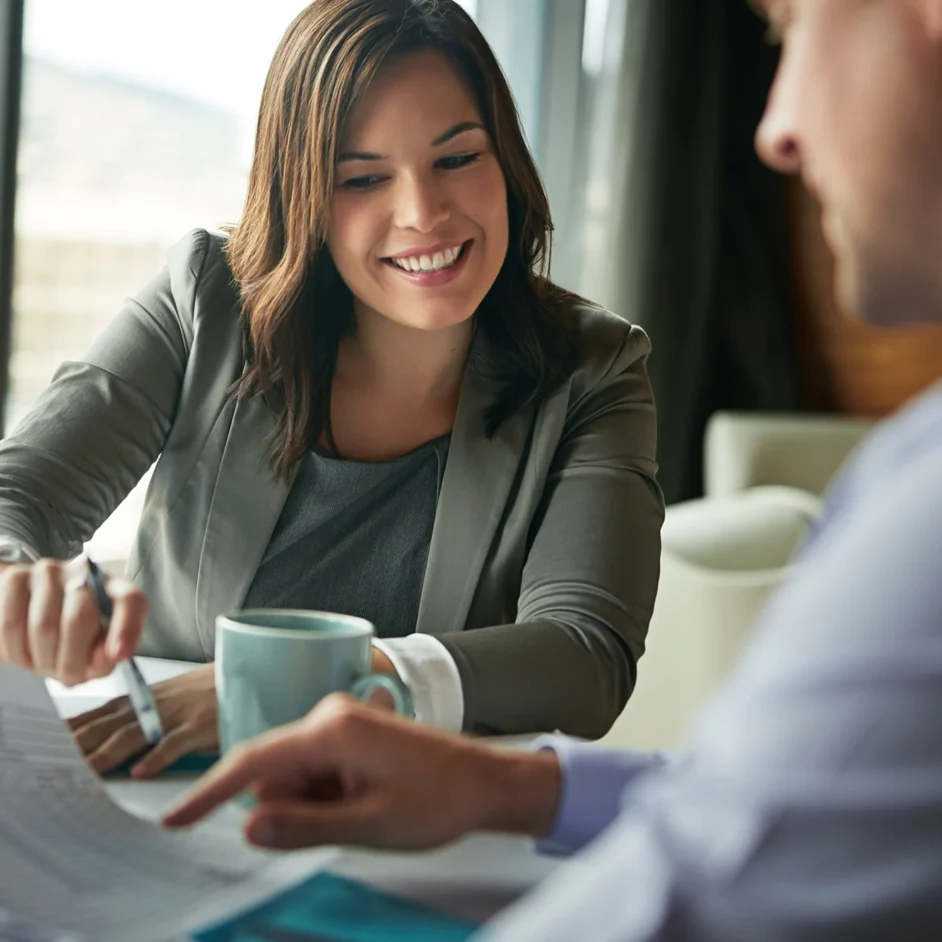 A woman and man sit at a table, reviewing paperwork together with focused expressions.