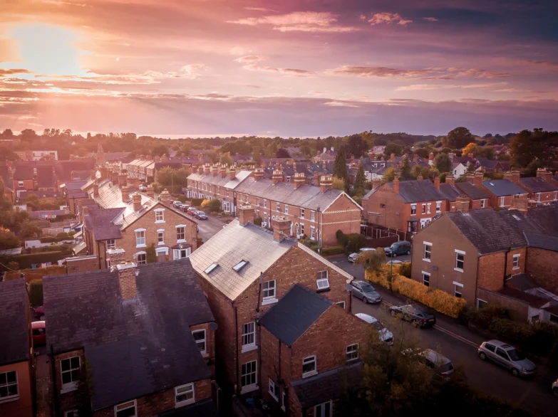 Aerial view of a residential area bathed in warm sunset hues, showcasing rooftops and streets below.