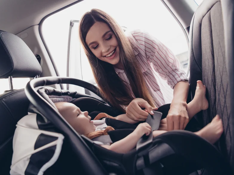 A woman gently holds a baby in a car seat, smiling warmly.