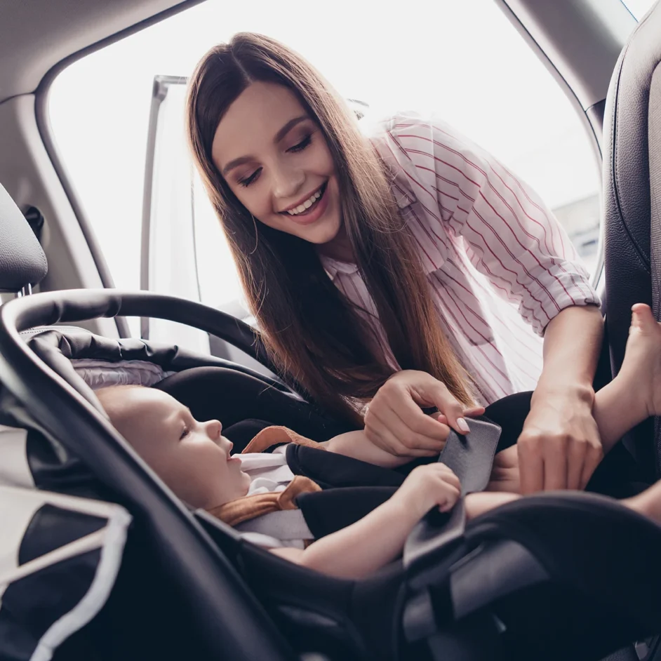 A woman gently holds a baby in a car seat, smiling warmly.