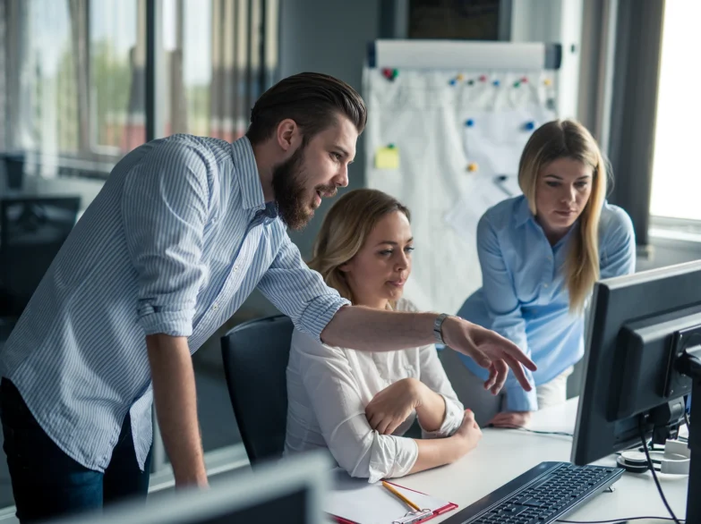 Three colleagues collaborating on a computer in a bright office space, sharing ideas and working together.