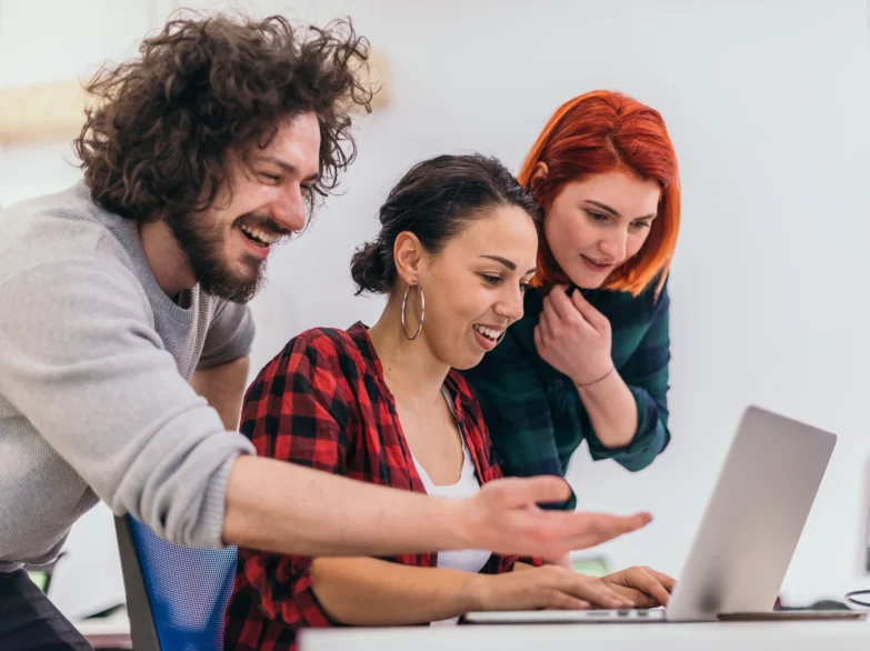 Three people gathered around a laptop, engaged in discussion while looking at the screen together.