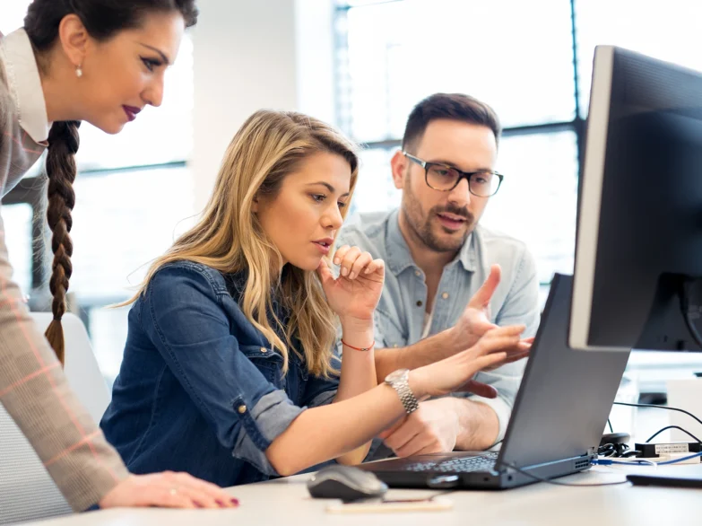 Three people gathered around a computer screen, engaged in discussion and looking at the display together.