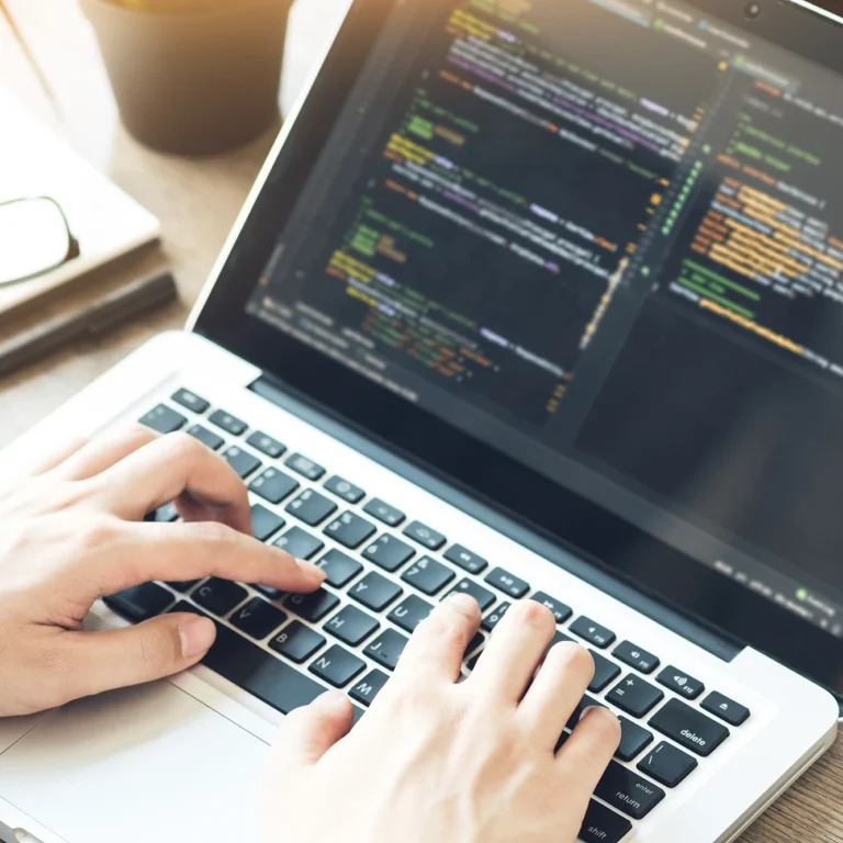 A person typing on a laptop displaying lines of code on the screen.