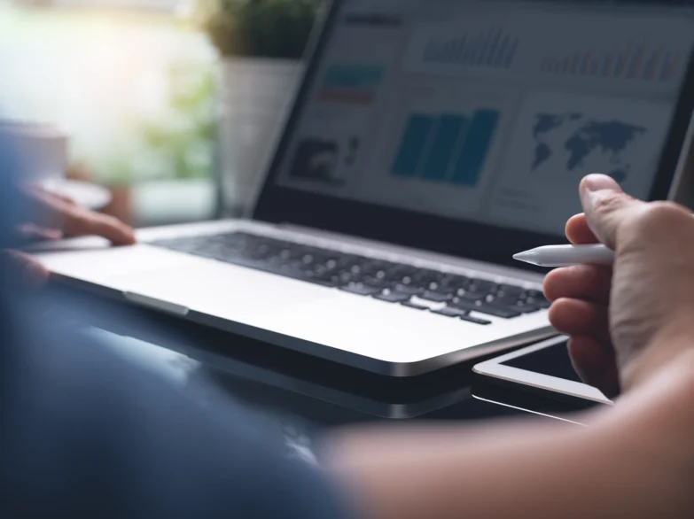 A person writes with a pen while working on a laptop computer at a desk.