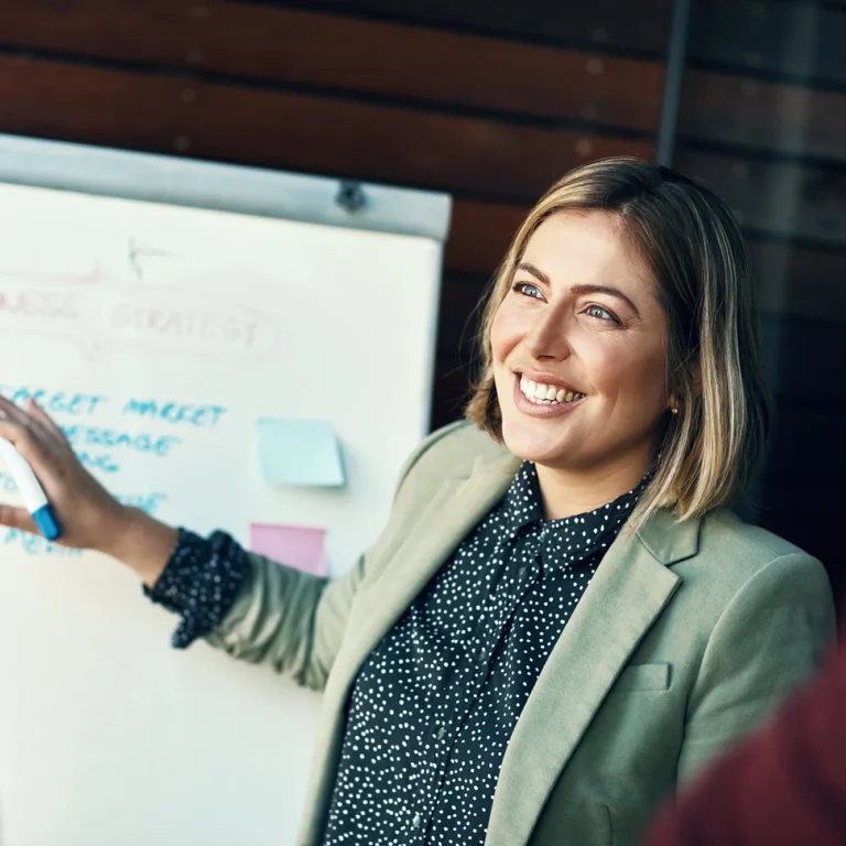 A woman stands by a whiteboard displaying a note, engaged in a discussion or presentation.
