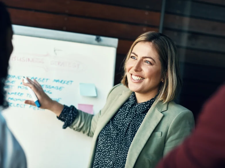 A woman stands by a whiteboard displaying a note, engaged in a discussion or presentation.