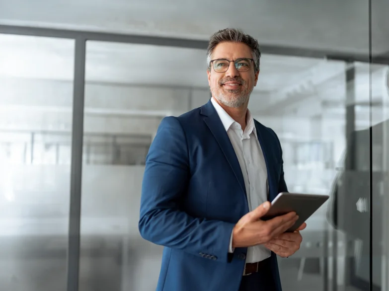 A man in a suit and glasses is holding a tablet, looking engaged and focused on the screen.