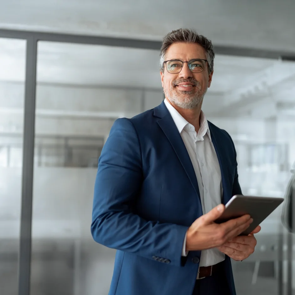 A man in a suit and glasses is holding a tablet, looking engaged and focused on the screen.