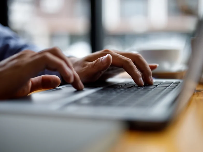 Close-up of hands typing on a laptop keyboard, focusing on fingers in motion and the laptop's screen.