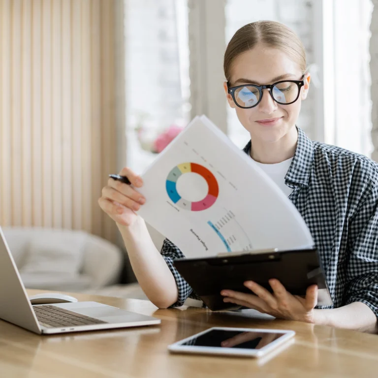 A woman in glasses studies a chart displayed on her laptop screen, focused and engaged in her work.