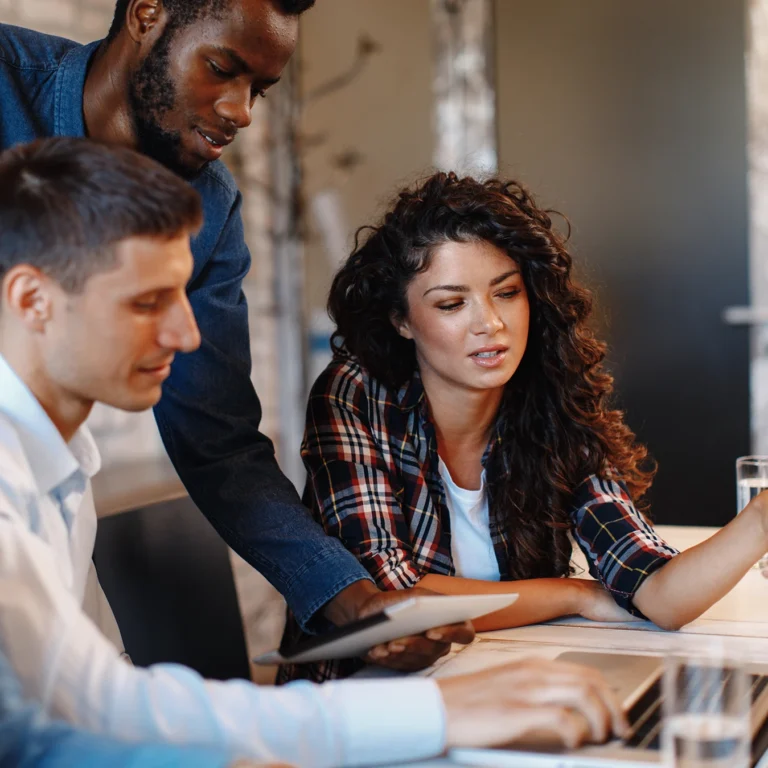 A diverse group of people gathered around a laptop, engaged in discussion and sharing ideas.