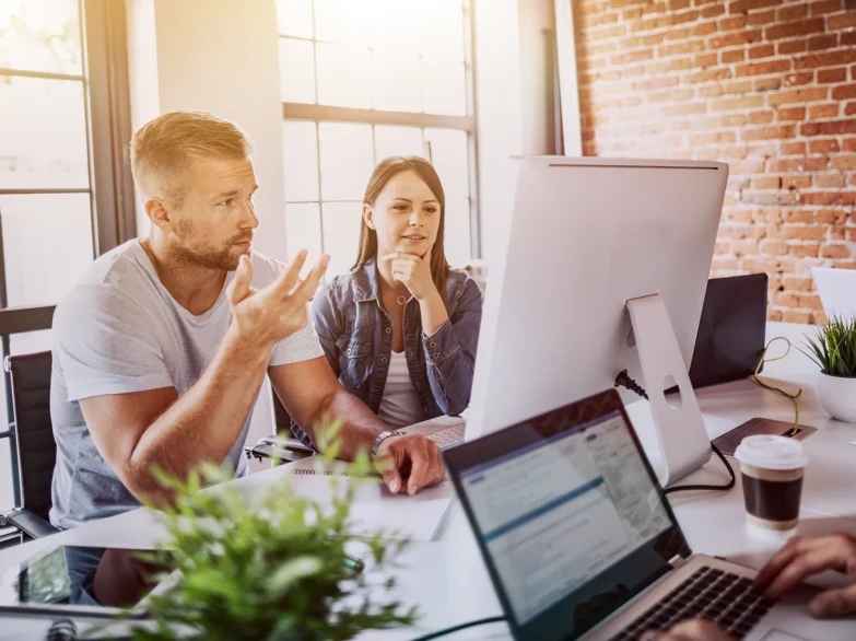Three people sitting at a table, each using a laptop, engaged in discussion and collaboration.