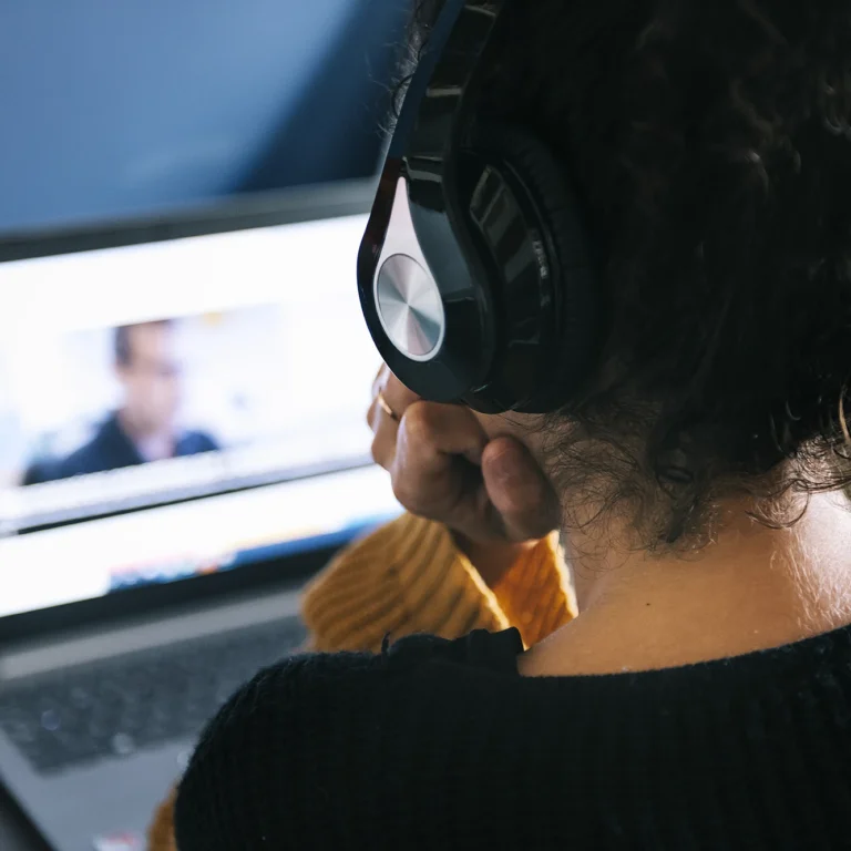 A woman with headphones watches a video on her laptop, focused and engaged in the content.